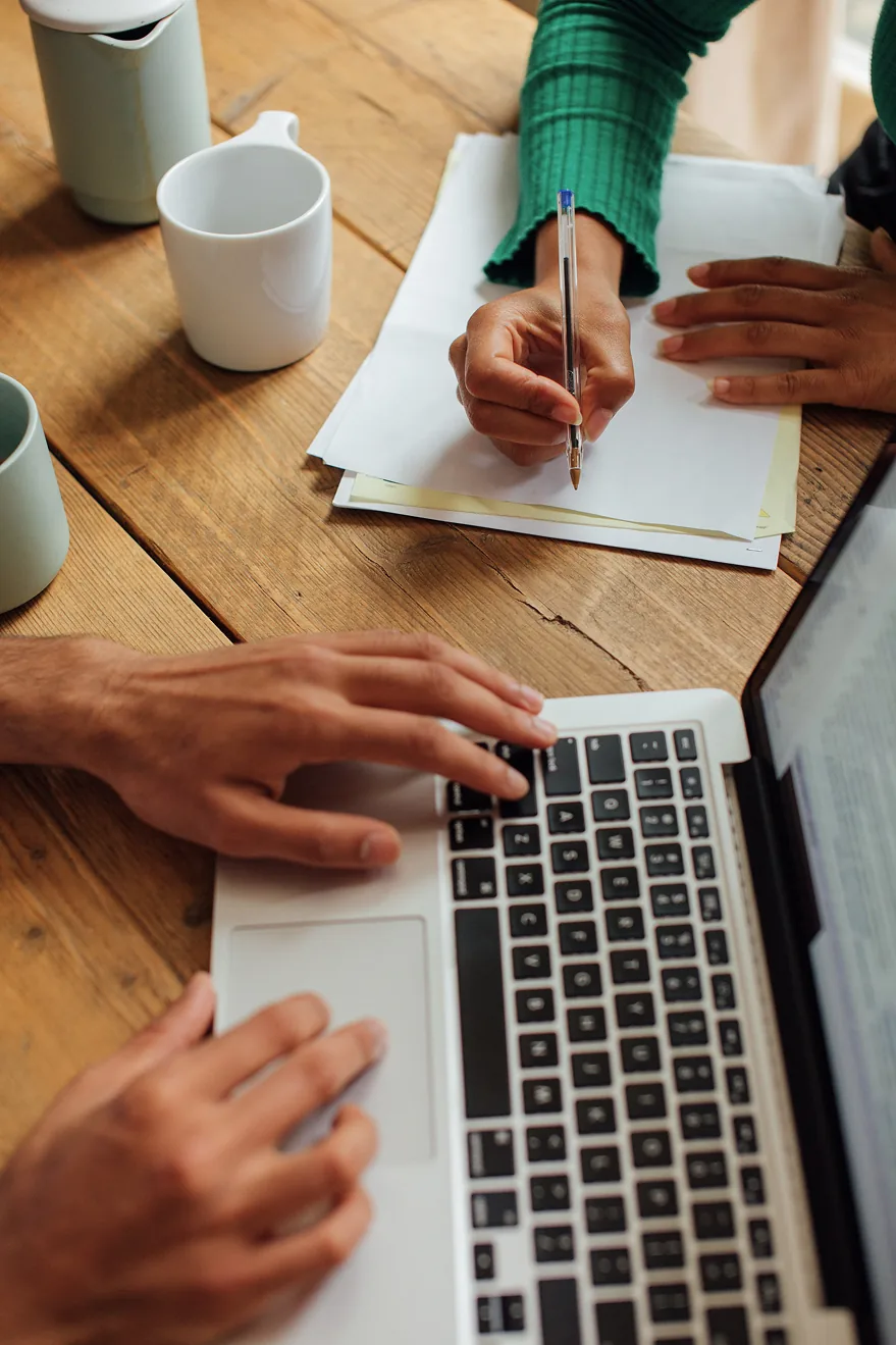 Two people making notes and typing on a laptop at a table