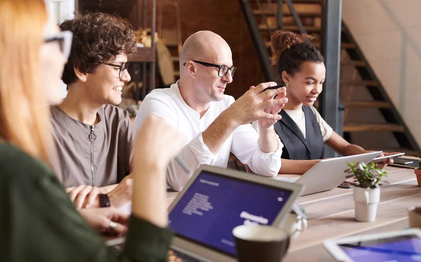 A diverse team discussing their work together at a table with laptops
